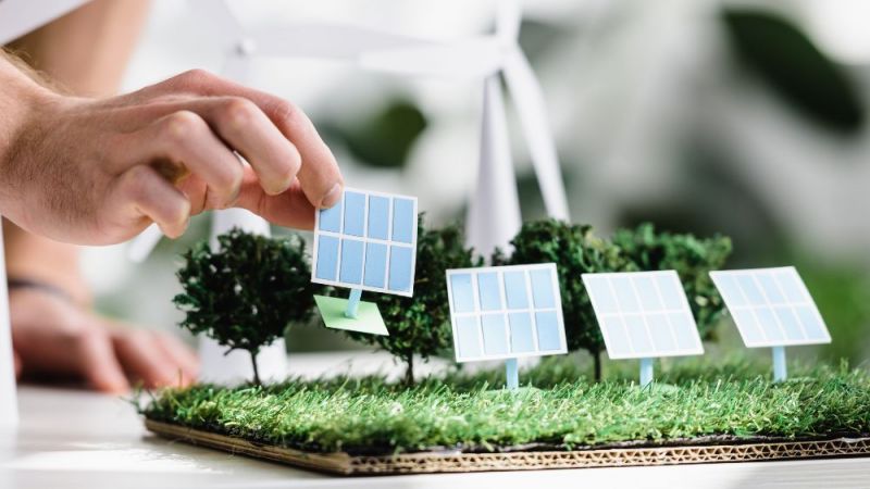 Es ist eine Hand zu sehen, die ein Modell eines Solarmoduls auf eine modellierte Grünfläche stellt.