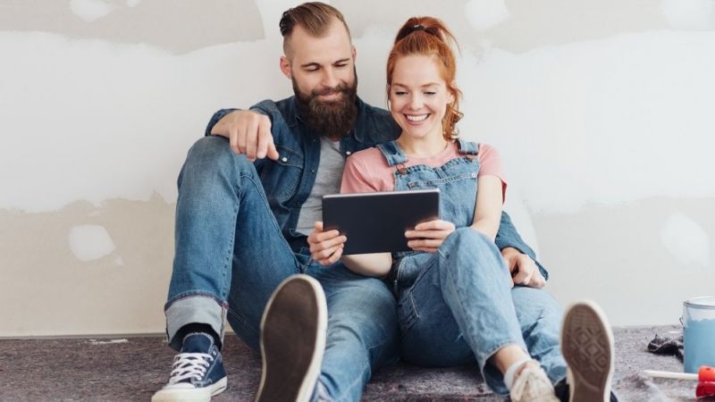 A couple looks at their tablet while renovating a flat.