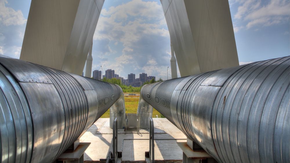 Pipelines for district heating can be seen in the foreground. A city can be seen behind them.