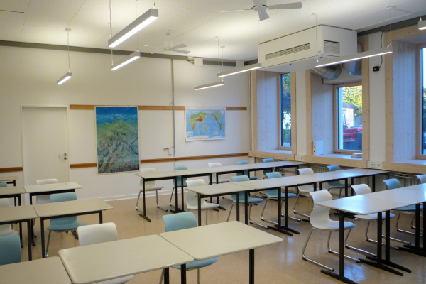 A classroom. The picture shows the deep window reveals due to the front façade and suspended, presence- and daylight-controlled luminaires. Here additionally with ceiling fans to investigate how these influence comfort.