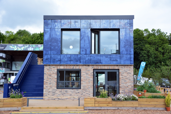 Ein Haus mit einer schimmernden dunkelblauen Fassade und großen Fenstern ist in der Frontalansicht zu sehen.